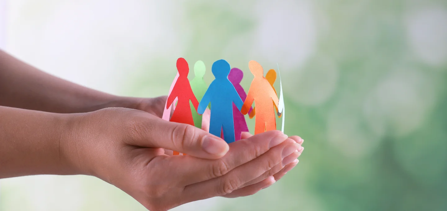 Hands holding cutouts of humans in different colours, linking hands.