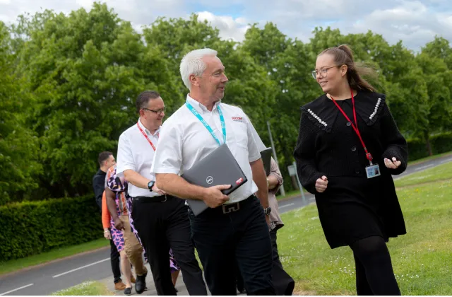 Red fading banner into an outdoor area with employees walking and smiling