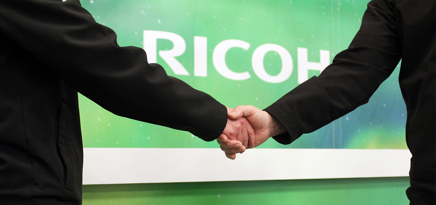 Two hands shaking in front of a green background with the Ricoh logo on