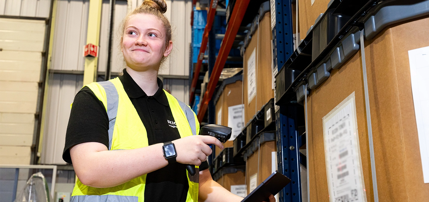 An employee in a high vis vest, in a warehouse, scanning a label